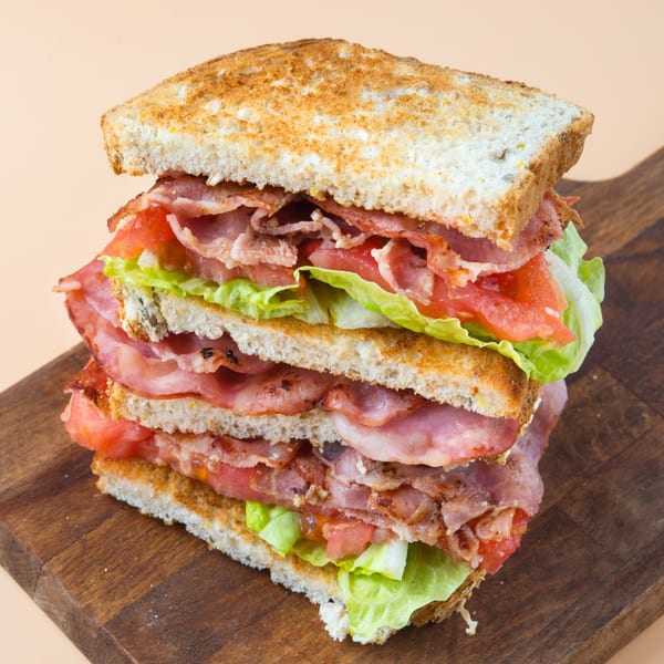 A tall, stacked BLT sandwich with toasted bread, bacon, lettuce, and tomato on a wooden board.