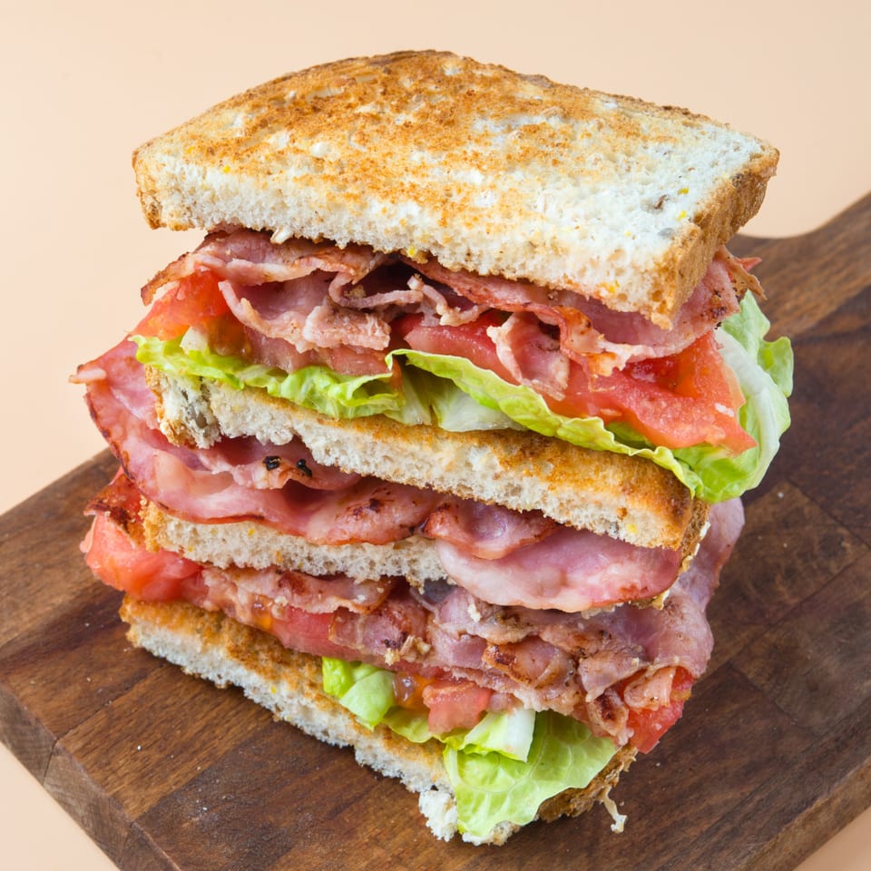 A tall, stacked BLT sandwich with toasted bread, bacon, lettuce, and tomato on a wooden board.