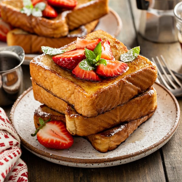 A stack of golden French toast with strawberries, powdered sugar, and mint on a plate.